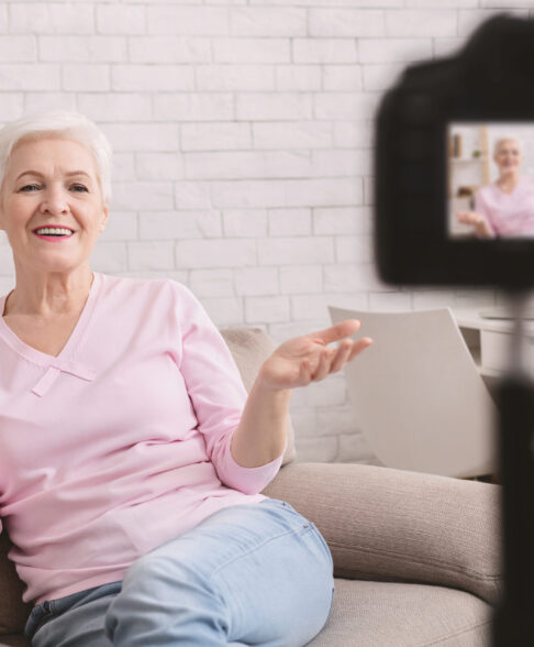 Experienced life coach. Friendly senior woman blogger sitting on sofa and recording video vlog at home
